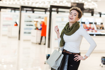 Happy blonde good-looking woman excited with shopping process standing with paper bags in light and airy hall of big mall