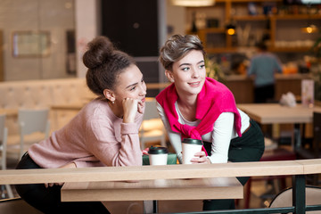 Two young female friends having coffee break together, having fun in shopping centre cafe. Holidays, shopping, relationships concept-Women enjoying companionship and coffee in mall food court.
