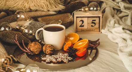 Christmas still life. Old vintage wooden calendar set on the 25 of December with cup with tea, cookies, oranges and nuts