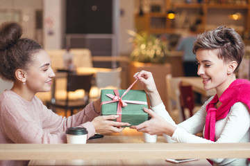 Young woman gets a gift box to her girlfriend - holidays or birthday celebrating, female friendship, homosexuality, same-sex marriage and love, modern lifestyle concept