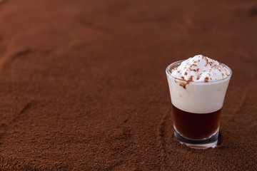 Little cup of piccolo latte macchiato on a table covered with ground coffee as a background