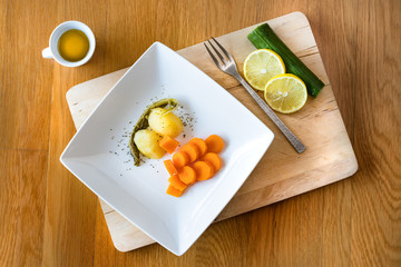 A plate with potatoes, cucumber, carrot, lemon, olive oil on a wooden table, top view.