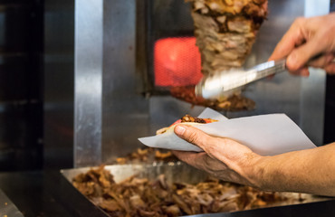 A man hand making a pita sandwich with pork gyros in a Greek restaurant.