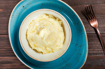 Bowl of mashed potatoes puree with butter on dark wooden background close up. Hot and healthy food, top view, flat lay