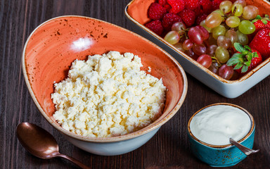 Fototapeta na wymiar Fresh cottage cheese with juicy berries raspberries, strawberry and grapes on dark wooden background. Dietary and healthy breakfast. Top view, flat lay