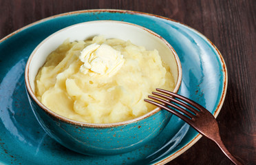 Bowl of mashed potatoes puree with butter on dark wooden background close up. Hot and healthy food, top view, flat lay
