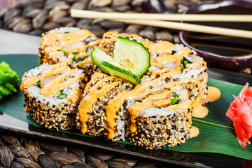 Sushi rolls set with shrimp tempura, cucumber, onion, avocado and sesame on black stone on bamboo mat, selective focus. Japanese cuisine