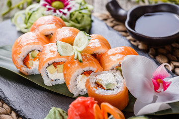 Sushi rolls set with salmon, cream cheese, red caviar, avocado and wasabi on black stone on bamboo mat, selective focus. Japanese cuisine