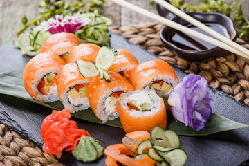 Sushi rolls set with salmon, cream cheese, red caviar, avocado and wasabi on black stone on bamboo mat, selective focus. Japanese cuisine