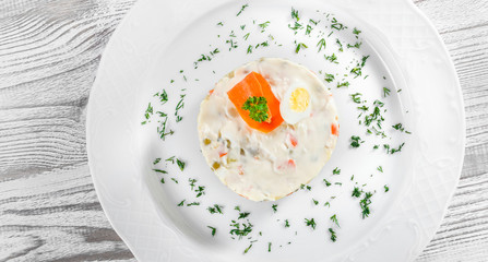 Traditional russian Christmas and New year salad Olivier with decoration on the plate on light wooden. Top view