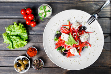 Greek salad of organic vegetables with tomatoes, cucumbers, red onion, olives, feta cheese and sweet pepper on wooden background. Healthy food. Top view