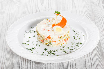 Traditional russian Christmas and New year salad Olivier with decoration on the plate on light wooden. Top view