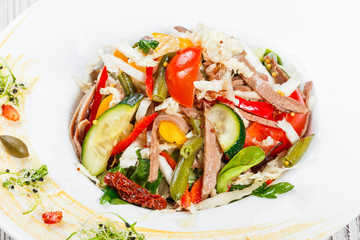 Fresh vegetable salad with cow tongue, spinach, green beans, tomatoes, sweet peppers, cabbage, mustard and dried tomatoes on plate on light wooden background. Healthy food. Top view