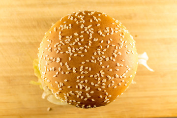 A large burger sprinkled with sesame top, cheese and salad. View from above