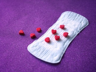 Sanitary napkin and red hearts on purple background