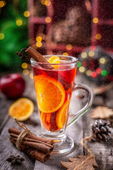 Glass of Christmas mulled red wine with spices and fruits surrounded by festive decoration,  on a wooden rustic table. Vertical composition