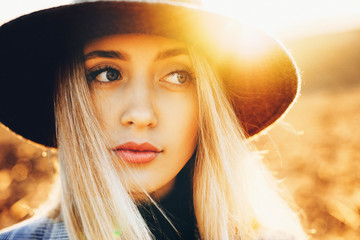 Lovely young female in elegant hat looking away while standing on blurred background of nature on amazing sunny day.Pretty lady looking away in countryside