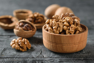Peeled walnut in a wooden bowl on a black wooden table.