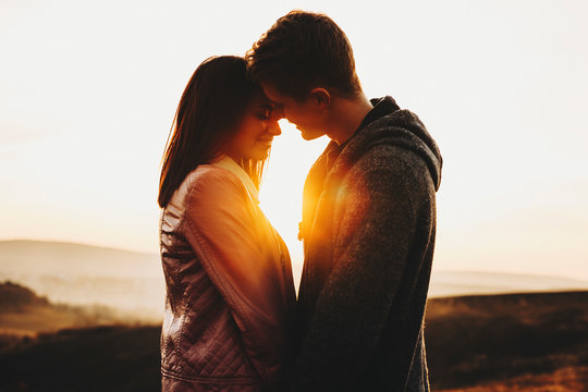 Side view of attractive young man and woman standing against sunset sky in wonderful countryside.Cute couple against sundown sky