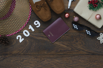 Table top view of Merry Christmas decorations & Happy new year 2019 ornaments concept.Flat lay essential difference objects to travel text & gift box with clothing  on modern wooden brown background.