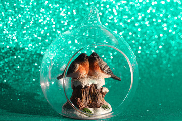 The couple of bullfinches sits on the snowy stump inside the glass transparent Christmas ball on a shining bokeh background. Christmas holiday concept