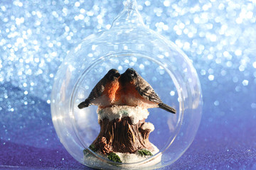 The couple of bullfinches sits on the snowy stump inside the glass transparent Christmas ball on a shining bokeh background. Christmas holiday concept