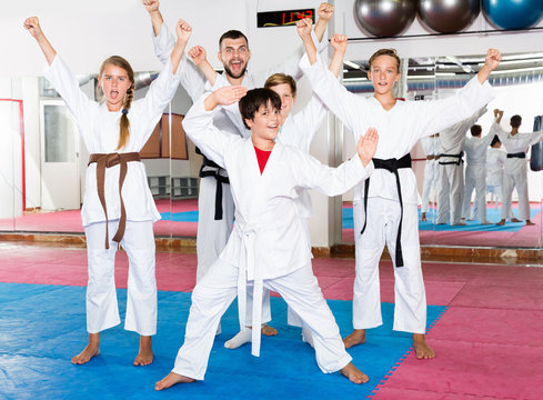 Group of emotional kids with man trainer posing in gym after taekwondo workout