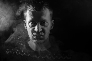 Monochrome portrait of a man who is angry and has bad emotions with a face mash and smoke around on a black isolated background. The face of the guy in the shade with color illumination.