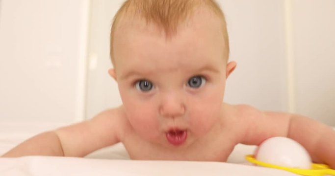 Four-month baby playing with a rattle and lying on stomach on a bed in a white room