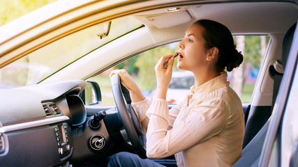 Woman using lipstick inside car. Urban background. Bad busy