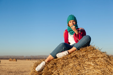 Naklejka na ściany i meble Fashion lifestyle portrait of young trendy woman dressed in warm stylish coat, knitting hat and jeans posing and smiling on yellow a stack of hay. portrait of joyful woman