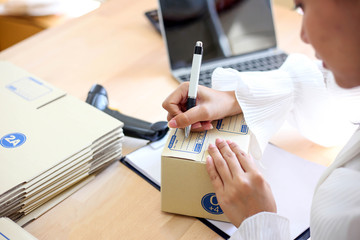 Young asian girl is freelancer Start up small business owner writing address on cardboard box at workplace,Shipping shopping online small business entrepreneur SME or freelance