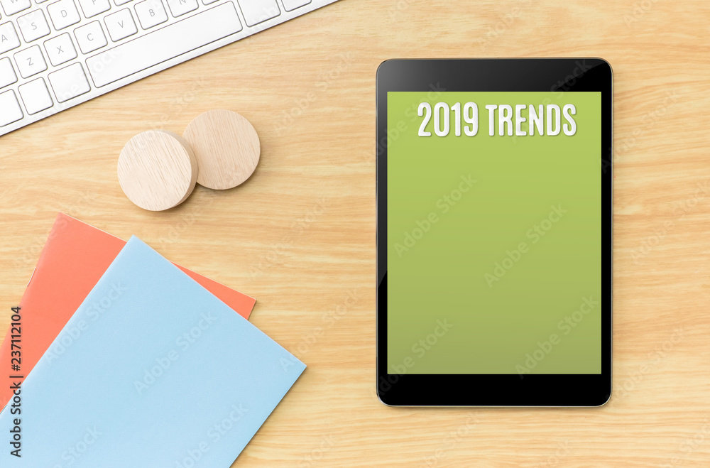 Poster 2019 trends on green screen tablet with blue notebook and keyboard on wooden table,new year resolutions.Mock up for display your content