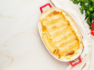 Cannelloni with filling of ricotta and parsley, baked with béchamel sauce, top view, copy space, white marble background