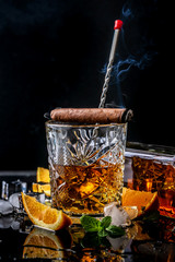 Glass of whiskey with smoking cigar and ice cubes on a black background. concept luxury drink...