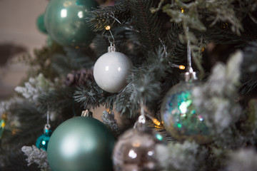 Christmas toys on a green artificial Christmas tree in a gentle style and gold lights garlands. Green, white and blue glass cones and balls decorate the spruce, close-up.