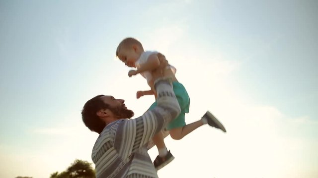 Strong father lobbed son in the sky. Playing with him at sunset in the wheat field