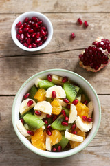 Salad of slices of various fruits and pomegranate seeds on a wooden background.