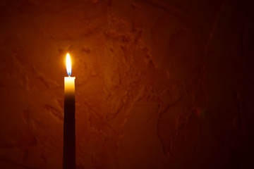 One yellow tall candle flame  burning on dark red blurred background with copy space for text. Advent or memorial prayer candle flame.