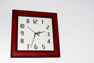 Square shape wall clock with white dial and red brown frame on very light grey background with copy space for text.