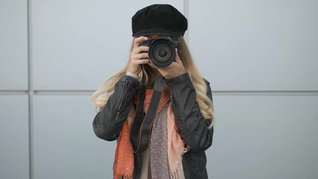 Professional young blonde woman photographer with digital camera taking pictures at city parking. Close Up, shallow depth of field, metal panels background.