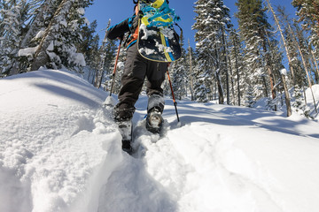 Asian man snowboarder freeride in snowshoes rises uphill in winter on snow