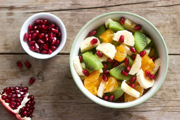 Salad of slices of various fruits and pomegranate seeds on a wooden background.