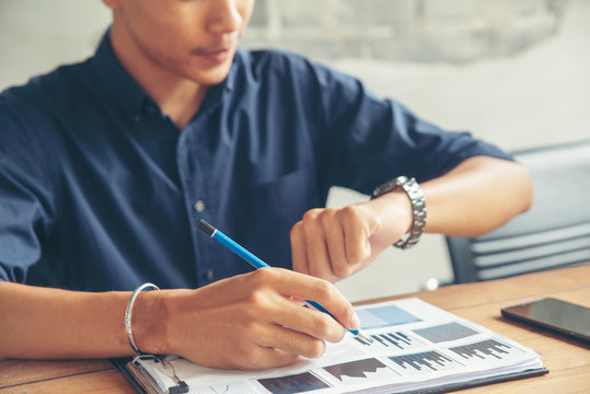Time out concept.Business man seeing wrist watch to check time at office.Boss look at clock to work.On Wooden desk with calendar,laptop,annual and summary report.It's Time out for appointment meeting.