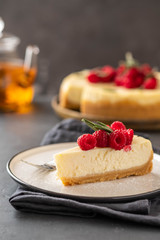 Slice of New York Cheesecake with raspberries on a dark background.