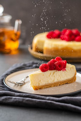Slice of New York Cheesecake with raspberries on a dark background.