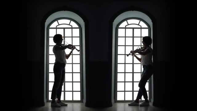 Girl plays the violin in the evening against the background of a window. Silhouette