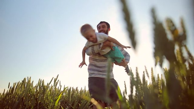 Close-up of father and son playing together. on the wheat field. Young father rotates his son in hands
