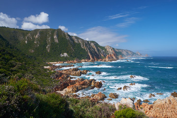 Fototapeta na wymiar Coastal landscape with green headlands, red rocks and rough seas in summer