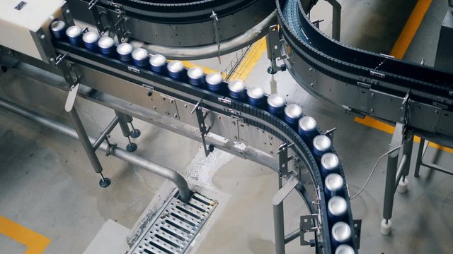 Beer cans are moving along the conveyor belt in a top view
